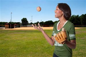 Smiling softball player tossing a ball around in her hands.